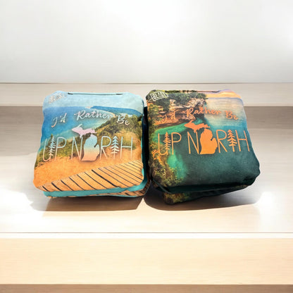 Two pillows with the text "I'D Rather Be UP NORTH" printed on them, sitting on a wooden surface.